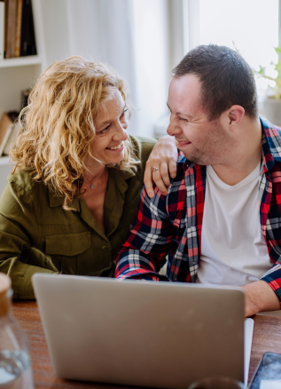 a woman and man with a disability on the computer, smiling at each other