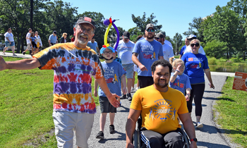 a group of people walk together and some roll in their wheelchairs on a sunny day in a park