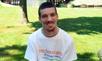 Cody smiles wearing an Easterseals MA T-shirt outside on a sunny day