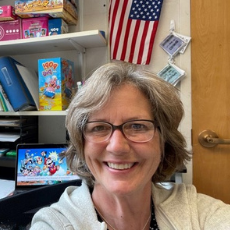 Doris smiles in her office, with a stack of games/tools used during services behind her