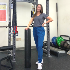 Kristina stands beside a large piece of physical therapy equipment and smiles