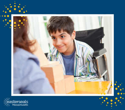 A young man sits in a wheelchair in front of a desk with wooden blocks used for physical therapy