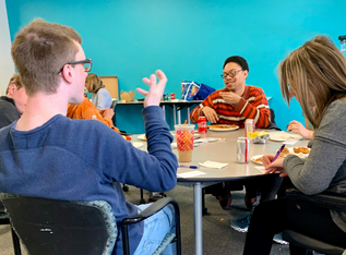 three young people gather at a table and eat snacks