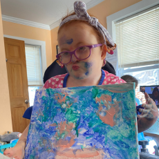 Sajjona sits and holds her painting up
