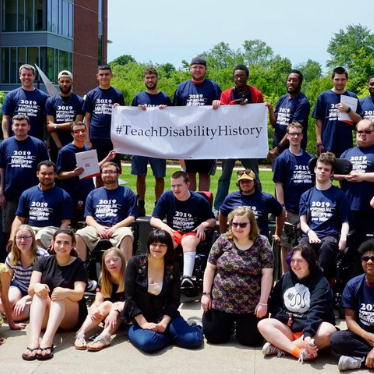 group of youth with disabilities outside holding a banner that says Teach Disability History
