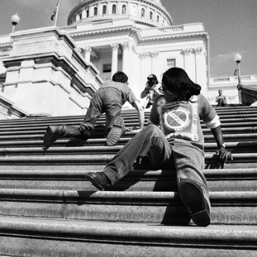 black and white photo of two young people with disabilities crawling up the stairs of the capital building