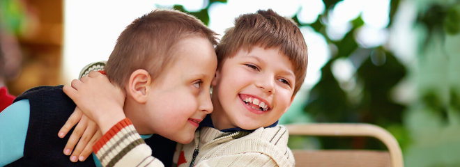 Two young boys with disabilities sit together and smile in a school setting