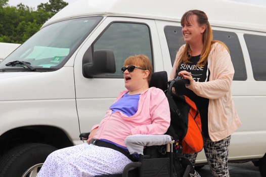 Two Women one in Wheelchair, wheeling in front of van smiling