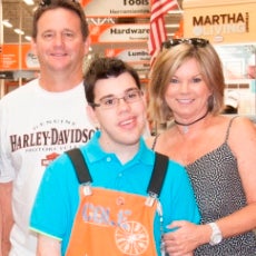 young man working at the home depot taking a picture with a couple behind him all smiling and looking at the camera