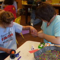 two children sitting at a table, making beaded necklaces