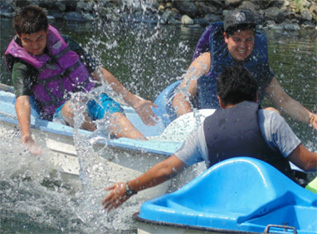 3 young men are in paddle-boats, splashing each other and smiling