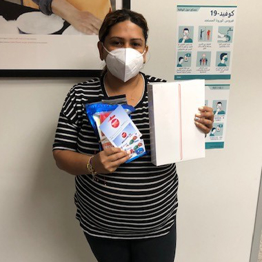 Connecting Communities Program participant, Angelica - wearing her safety mask, holding some supplies given to her by our program (including an iPad)