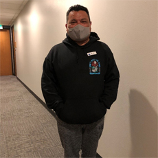 Connecting Communities Program participant, Juan H. Becerril, smiling in the hallway of our office, wearing a mask.