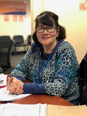 Connecting Communities Program participant, smiling while sitting at a desk, in class.