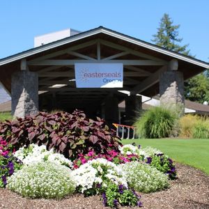 Easterseals Oregon banner hangs from a building, over some flowers, at a golf course.