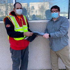 Participant Paul is standing with Employment Specialist, Ryan. They are at Pauls' workplace, Portland International Airport. They are both holding a piece of Paul's new uniform together, in celebration.