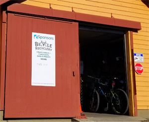 Barn door is open, revealing the entrance to a bicycle repair shop. An exterior sign reads "Sponsors Bicycle Recyclery," followed by text that is too small to read in the photo.