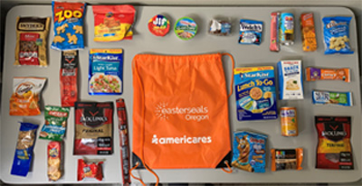 Orange drawstring bag reads "AmeriCares and Easterseals Oregon." The bag is surrounded by numerous food items neatly laid out on a table.