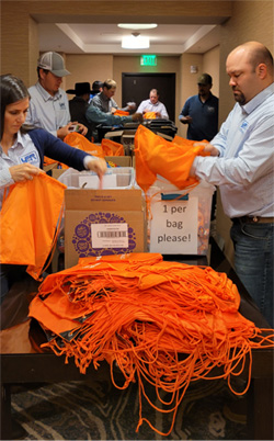 A line of volunteers are surrounding a table, filling drawstring bags with various food.