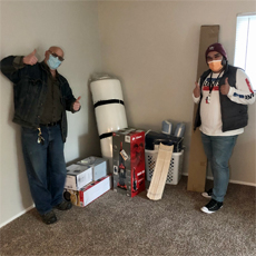 Supportive Services for Veteran Families participant Robert Webb, standing in his new apartment home, with his case manager. They are both wearing protective masks and giving a 
