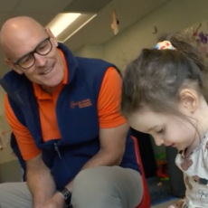Man sitting next to a girl smiling while she colors