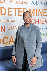 Angela wearing a grey jacket, standing in front of the word wall.