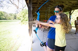 A young girl learning archery with a camp counselor.