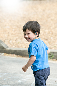 A young boy wearing a hearing aid looks to his left