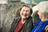 Two elderly women on a couch smiling at one another