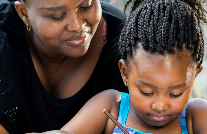 an instructor looks over the shoulder of a young child as she completes homework at a table