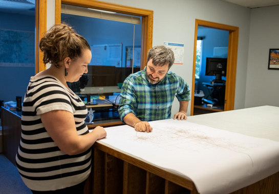 A man and woman looking at transportation plans on a table