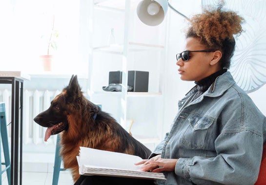 A blind woman reading braille, with her service animal 