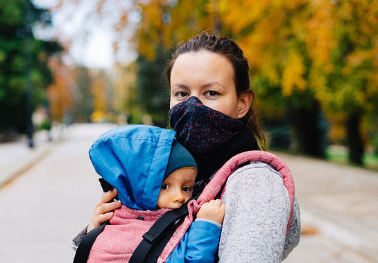 A woman in the street wearing a mask, holding a baby 