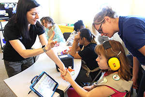 A girl and two troop leaders read the Girl Scouts pledge using an iPad