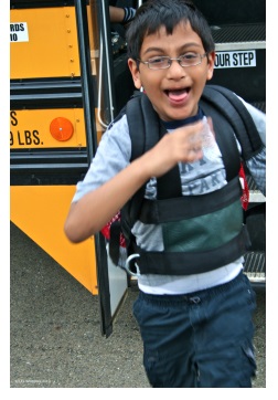 a young male child smiling in mid-run with a school bus behind him