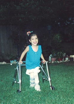 Kelley as a child, walking across a lawn using a walker