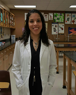 Kelley in front of her classroom wearing a white lab coat