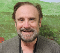 Ken smiling for the camera in front of a painting of a landscape