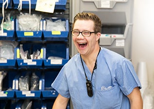 A young man smiling wearing blue scrubs