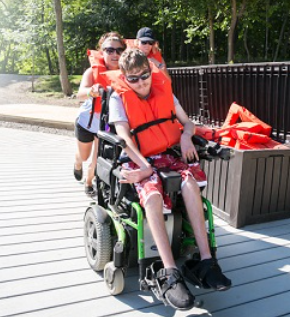 A teen in a life jacket being pushed on a dock by a camp counselor.