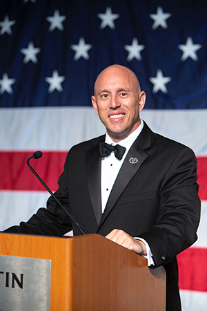 Tim wearing a tuxedo at a podium in front of an American flag