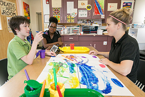 Two volunteers painting with a young child.