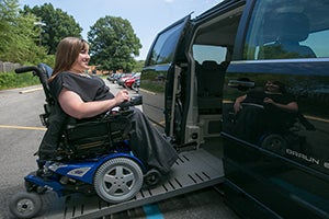 A woman in a wheelchair using a ramp to board a van