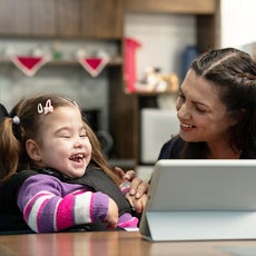 Woman and girl playing with tablet on the table in front of them.