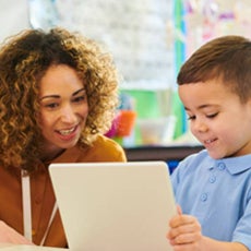 A black teacher with brown and blonder curly hair teaches a student how to use an AAC Tablet