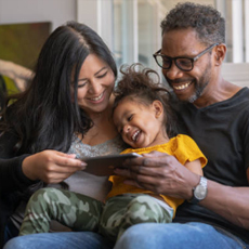 An interracial family interacting with their toddler using an AAC tablet 