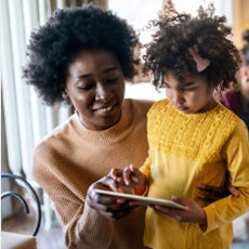 A black mom and son smiling while learning how to navigate the AAC tablet 