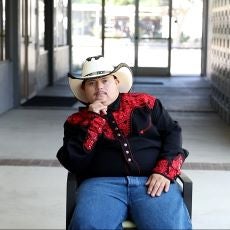 Jose dressed in his mariachi hat and shirt sitting in a chair. 