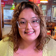 Blonde woman with glasses smiling while sitting in a booth at a restaurant