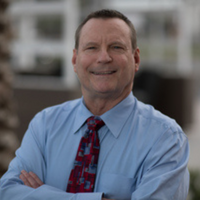 White male with sandy brown hair and long sleeve blue shirt with red tie smiling